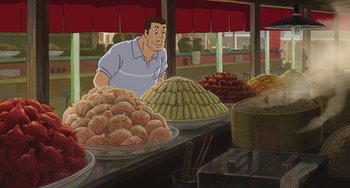 Movie still from “Spirited Away” (2001), directed by Hayao Miyazaki – A man standing in front of a table filled with food; Medium shot, High angle