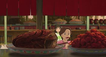 Movie still from “Spirited Away” (2001), directed by Hayao Miyazaki – A woman and a child in front of a table full of food; Medium shot, High angle