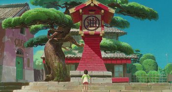Movie still from “Spirited Away” (2001), directed by Hayao Miyazaki – A person standing in front of a building with a clock on it; Extreme Wide shot, Low angle
