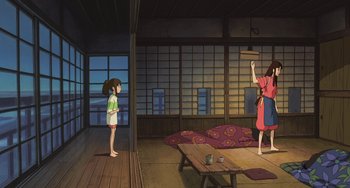 Movie still from “Spirited Away” (2001), directed by Hayao Miyazaki – A woman in a red dress is standing in front of a girl; Wide shot, Low angle