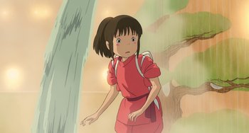 Movie still from “Spirited Away” (2001), directed by Hayao Miyazaki – A girl in a red dress standing next to a tree; Medium shot, Low angle