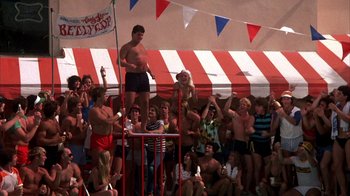 Movie still from “Spring Break” (1983), directed by Sean S. Cunningham – A crowd of people watching a man on a stilts; Wide shot, High angle