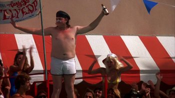 Movie still from “Spring Break” (1983), directed by Sean S. Cunningham – A man and a woman are standing in front of a crowd; Medium shot, Low angle