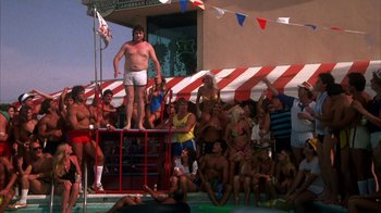 Movie still from “Spring Break” (1983), directed by Sean S. Cunningham – A man standing on top of a red and white pole; Wide shot, Low angle