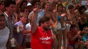 Movie still from “Spring Break” (1983), directed by Sean S. Cunningham – A man singing into a microphone in front of a group of people; Medium shot, Low angle
