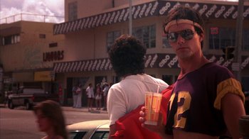 Movie still from “Spring Break” (1983), directed by Sean S. Cunningham – A man holding a drink while standing next to a woman; Medium shot, Low angle