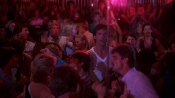 Movie still from “Spring Break” (1983), directed by Sean S. Cunningham – A group of people are gathered together in a room; Medium shot, Over the shoulder angle