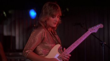 Movie still from “Spring Break” (1983), directed by Sean S. Cunningham – A woman in a gold dress playing a guitar; Medium shot, Low angle