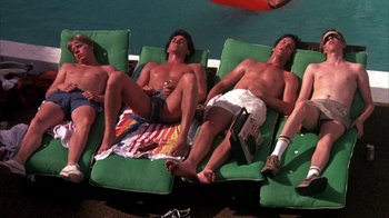 Movie still from “Spring Break” (1983), directed by Sean S. Cunningham – A group of men laying on lounge chairs next to a swimming pool; Wide shot, Overhead angle