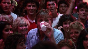 Movie still from “Spring Break” (1983), directed by Sean S. Cunningham – A group of young people gathered around a man drinking from a paper cup; Close Up shot, Low angle