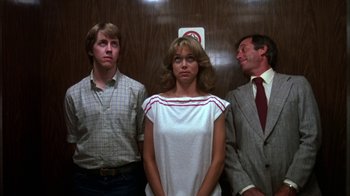 Movie still from “Spring Break” (1983), directed by Sean S. Cunningham – A woman standing next to two men in an elevator; Medium shot, Low angle