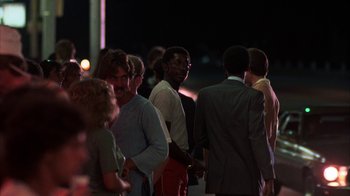 Movie still from “Spring Break” (1983), directed by Sean S. Cunningham – A group of people standing next to each other on the street; Medium shot, Over the shoulder angle