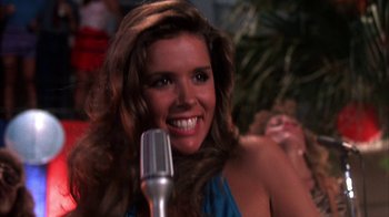 Movie still from “Spring Break” (1983), directed by Sean S. Cunningham – A woman smiles while holding a microphone; Close Up shot, Low angle