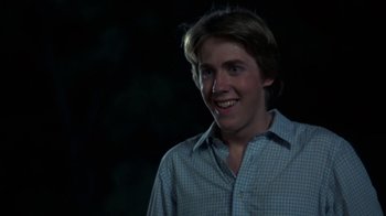 Movie still from “Spring Break” (1983), directed by Sean S. Cunningham – A young man smiling for the camera in the dark; Close Up shot, Over the shoulder angle