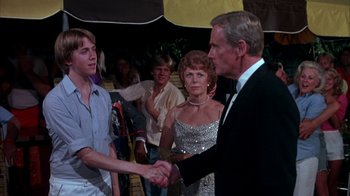 Movie still from “Spring Break” (1983), directed by Sean S. Cunningham – A man and a woman shaking hands in front of a crowd; Medium shot, Over the shoulder angle
