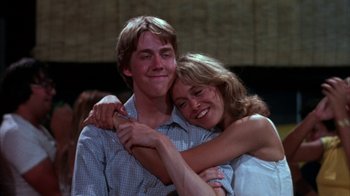 Movie still from “Spring Break” (1983), directed by Sean S. Cunningham – A man and a woman hugging each other in front of a crowd; Medium shot, Low angle