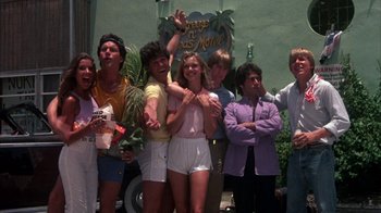 Movie still from “Spring Break” (1983), directed by Sean S. Cunningham – A group of people standing next to each other in front of a hotel; Wide shot, Low angle