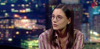 Movie still from “Squared Love All Over Again” (2023), directed by Filip Zylber – A woman wearing glasses sitting in front of lights; Close Up shot, Over the shoulder angle