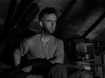 Movie still from “Stalag 17” (1953), directed by Billy Wilder – A black and white photo of a man sitting on a chair; Close Up shot, Low angle