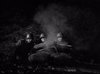Movie still from “Stalag 17” (1953), directed by Billy Wilder – A group of men sitting on top of a dirt field; Medium shot, Low angle