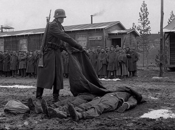 Movie still from “Stalag 17” (1953), directed by Billy Wilder – An old photo of a man holding a blanket over a dead body; Wide shot, Over the shoulder angle