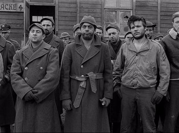 Movie still from “Stalag 17” (1953), directed by Billy Wilder – A group of men standing next to each other in front of a building; Medium shot, Over the shoulder angle