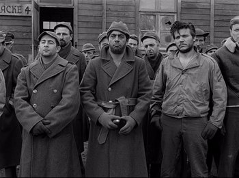 Movie still from “Stalag 17” (1953), directed by Billy Wilder – A group of men standing next to each other in front of a building; Medium shot, Low angle