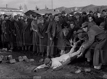 Movie still from “Stalag 17” (1953), directed by Billy Wilder – A group of men standing next to each other near a fence; Wide shot, High angle