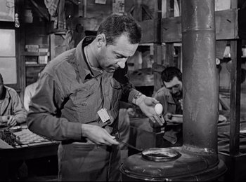 Movie still from “Stalag 17” (1953), directed by Billy Wilder – A man in an industrial setting using an old fashioned stove; Medium shot, Low angle