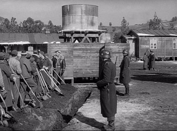 Movie still from “Stalag 17” (1953), directed by Billy Wilder – A black and white photo of a group of men standing next to each other; Wide shot, Over the shoulder angle