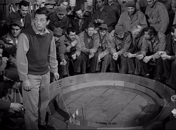 Movie still from “Stalag 17” (1953), directed by Billy Wilder – A group of men sitting in front of each other; Wide shot, High angle