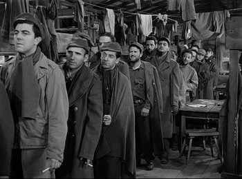 Movie still from “Stalag 17” (1953), directed by Billy Wilder – A black and white photo of a group of men standing together; Medium shot, High angle