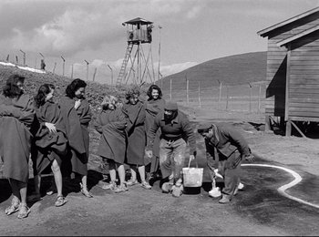 Movie still from “Stalag 17” (1953), directed by Billy Wilder – A group of people standing in a dirt field next to barbed wire fence; Wide shot, High angle