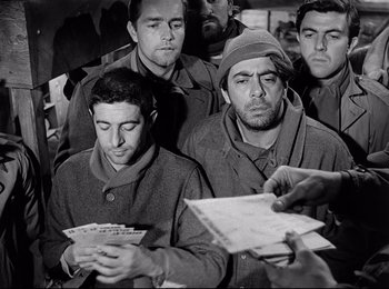 Movie still from “Stalag 17” (1953), directed by Billy Wilder – A black and white photo of a group of men looking at a piece of paper; Medium shot, Low angle