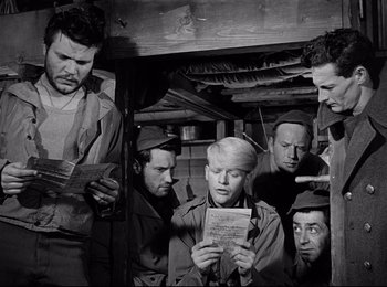 Movie still from “Stalag 17” (1953), directed by Billy Wilder – A black and white photo of a group of men looking at a piece of paper; Medium shot, Low angle