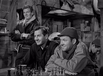 Movie still from “Stalag 17” (1953), directed by Billy Wilder – A group of men sitting next to each other on top of a chess board; Medium shot, High angle