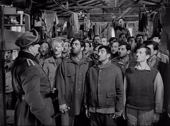 Movie still from “Stalag 17” (1953), directed by Billy Wilder – A group of men standing next to each other in a room; Wide shot, Low angle