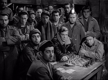 Movie still from “Stalag 17” (1953), directed by Billy Wilder – A black and white photo of a group of men sitting at a table; Medium shot, High angle
