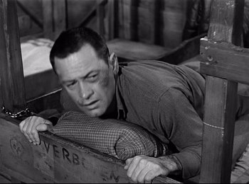 Movie still from “Stalag 17” (1953), directed by Billy Wilder – A black and white photo of a man leaning on a crate; Close Up shot, Low angle