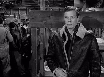 Movie still from “Stalag 17” (1953), directed by Billy Wilder – A black and white photo of a man in a leather jacket; Medium shot, Over the shoulder angle