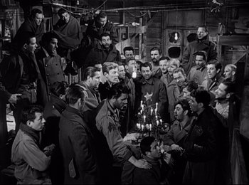 Movie still from “Stalag 17” (1953), directed by Billy Wilder – A group of men standing around a table with candles on it; Wide shot, High angle