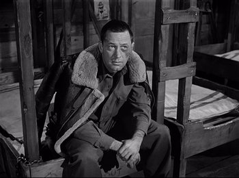 Movie still from “Stalag 17” (1953), directed by Billy Wilder – A man sitting on the ground wearing a jacket and a tie; Medium shot, High angle