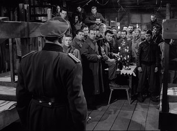 Movie still from “Stalag 17” (1953), directed by Billy Wilder – A group of men standing in front of a table with candles; Wide shot, High angle