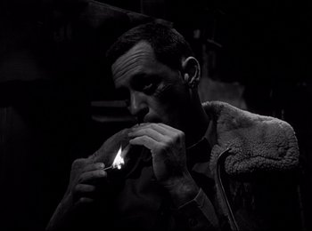 Movie still from “Stalag 17” (1953), directed by Billy Wilder – A black and white photo of a man lighting a cigarette; Close Up shot, High angle