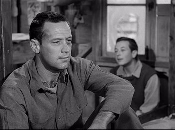 Movie still from “Stalag 17” (1953), directed by Billy Wilder – A man sitting next to another man on a couch; Close Up shot, Low angle