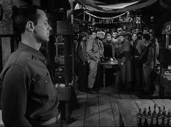 Movie still from “Stalag 17” (1953), directed by Billy Wilder – A group of men standing around a table; Medium shot, Over the shoulder angle