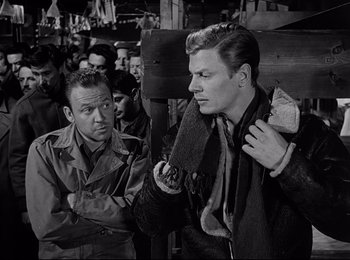 Movie still from “Stalag 17” (1953), directed by Billy Wilder – A man in a trench coat is talking to another man in a trench coat; Medium shot, Over the shoulder angle