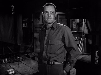 Movie still from “Stalag 17” (1953), directed by Billy Wilder – A black and white photo of a man standing in a room; Medium shot, Low angle