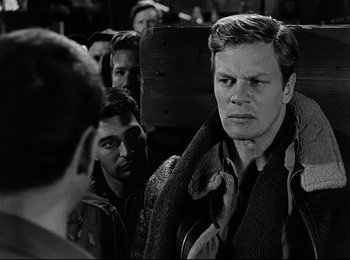Movie still from “Stalag 17” (1953), directed by Billy Wilder – Black and white photograph of a man in a crowd; Close Up shot, Over the shoulder angle