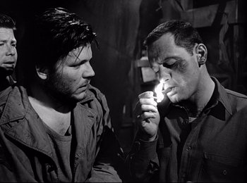 Movie still from “Stalag 17” (1953), directed by Billy Wilder – Two men are lighting a cigarette in a dark room; Close Up shot, Over the shoulder angle